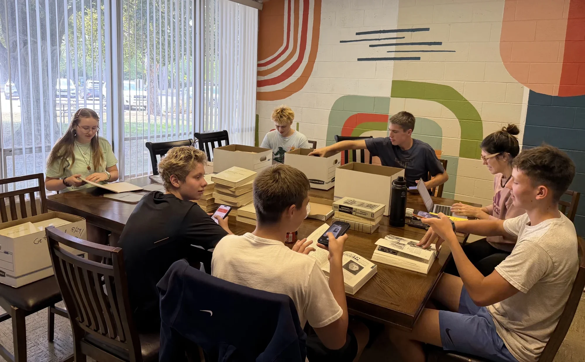 Young people cataloguing Lithuanian books with their phones at a table